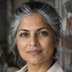 Portrait of a woman with silver-streaked hair in a linen shirt against an exposed brick wall.